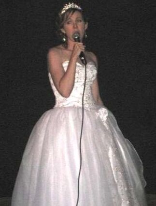 Rachel Moore, wearing a white dress, sings karaoke