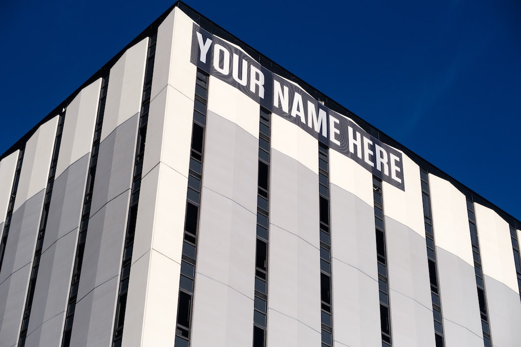 A gray and white building rises up against a dark blue sky. A black banner with white letters says: 